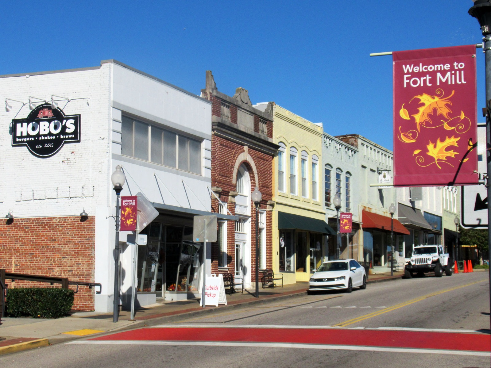 Storefronts along Main Street in downtown Fort Mill, South Carolina, with a maroon Welcome to Fort Mill pole banner and parked cars