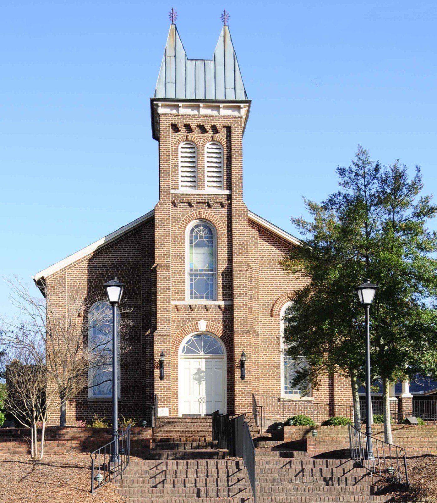 Historic red brick church with a tall central bell tower and twin metal spires under a clear blue sky in Fort Mill, South Carolina