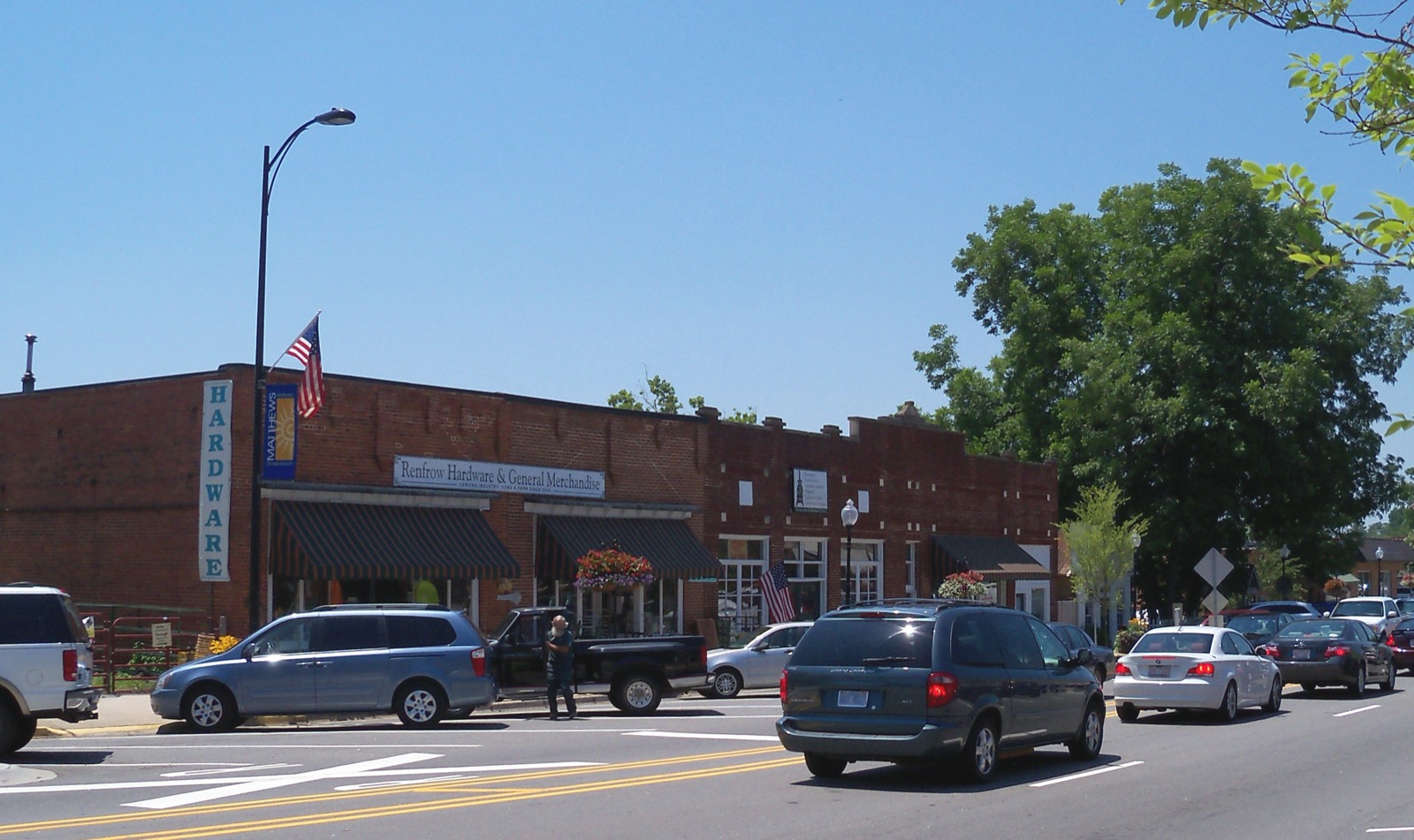 Brick storefront of Renfrow Hardware and General Merchandise on North Trade Street in downtown Matthews, North Carolina, with a vertical HARDWARE sign and a Matthews town banner on the lamp post