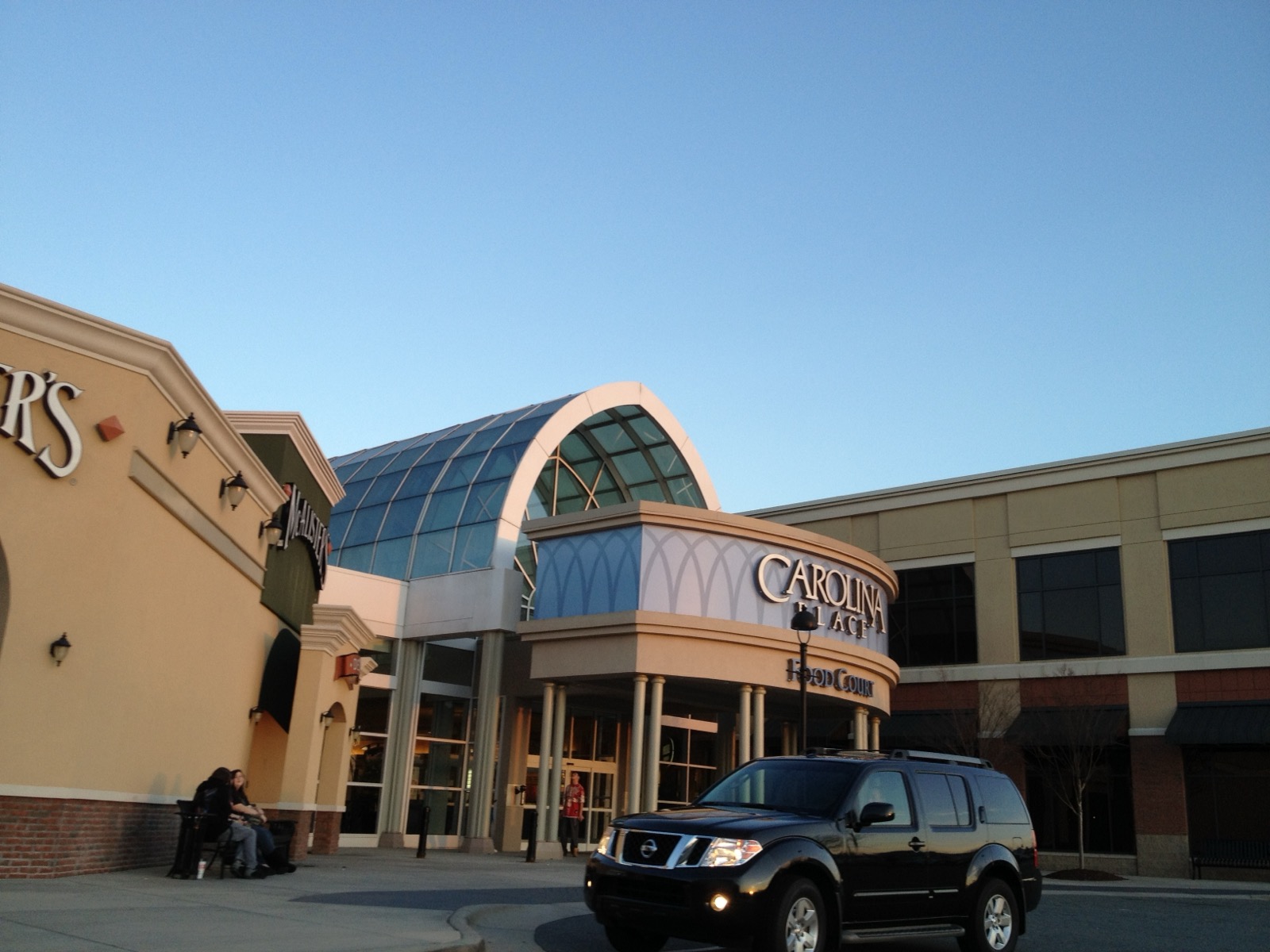 Glass-domed main entrance of Carolina Place Mall in Pineville, North Carolina, at dusk with cars in the parking lot