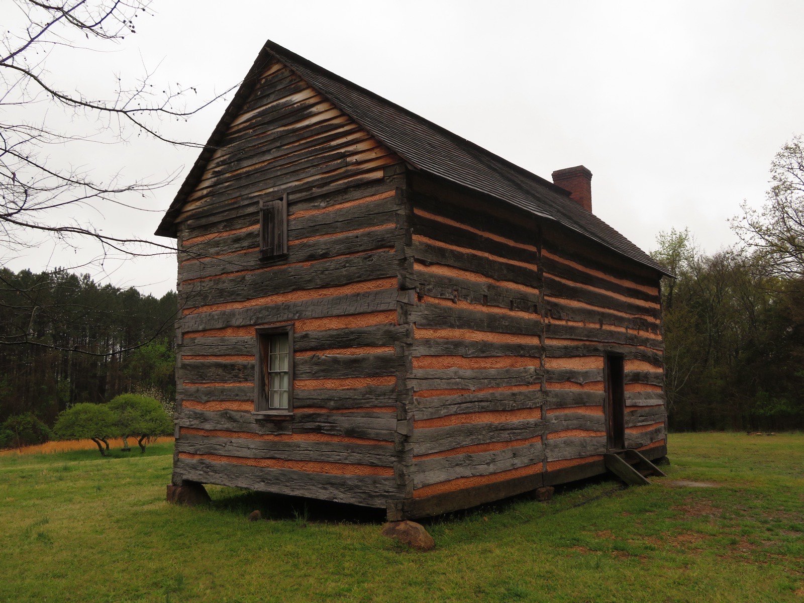 Weathered two-story log cabin with a brick chimney on a green lawn at the President James K. Polk birthplace site in Pineville, North Carolina