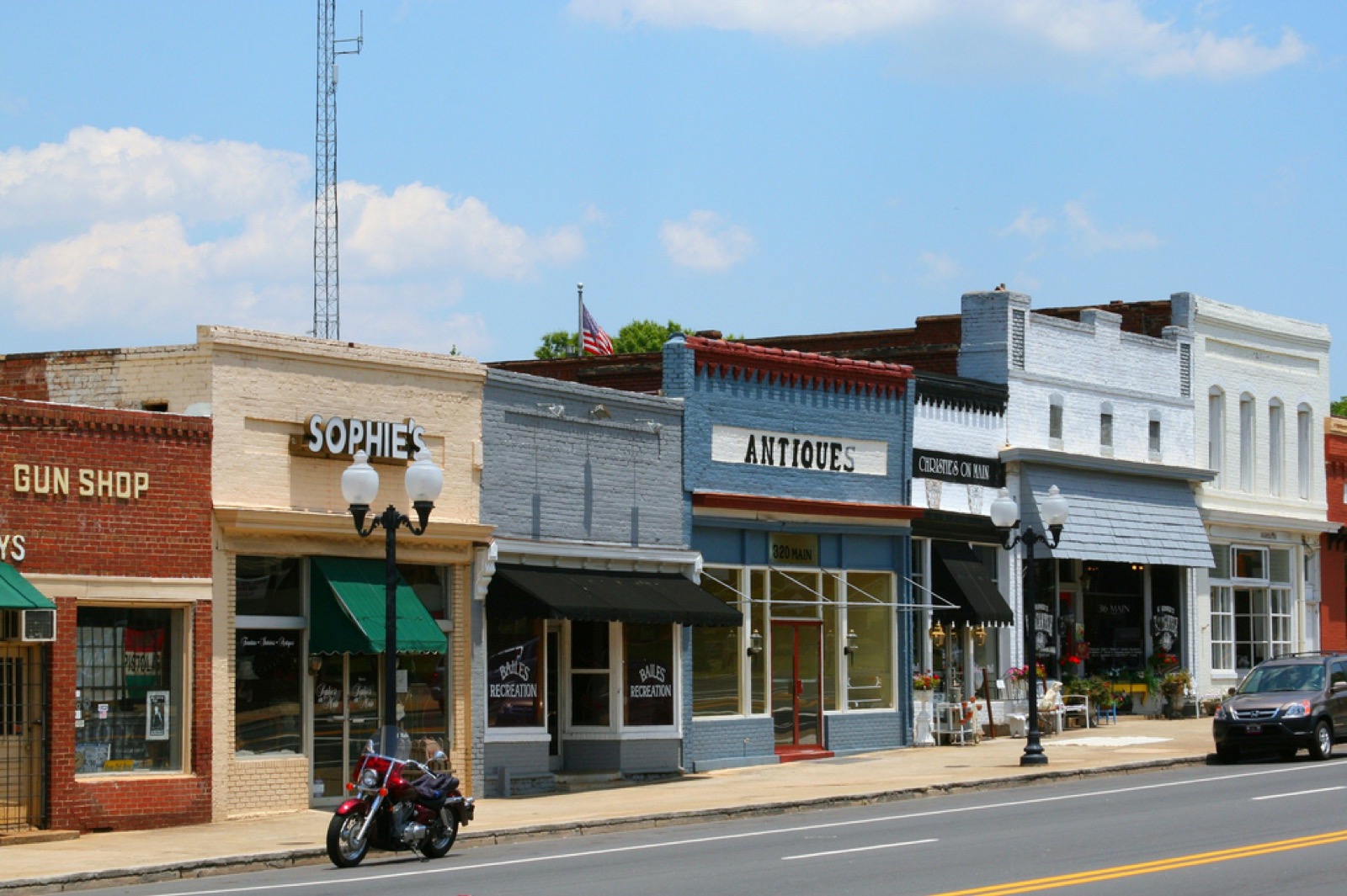 Row of brick and painted storefronts on Main Street in downtown Pineville, North Carolina, including an antiques shop and a motorcycle parked at the curb